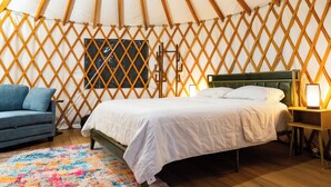A yurt interior with a bed, a blue sofa, a colorful rug, and a wooden lattice wall. - New Leaf Greenhouse (Cornelius)