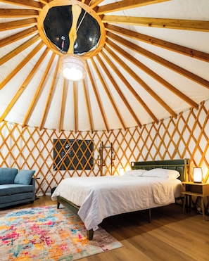 Interior de una yurta con cama, sofá azul, alfombra colorida y pared de celosía de madera.