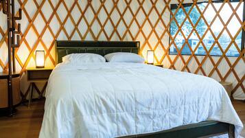 Een bed in een tent met een kleurrijk vloerkleed, houten latenwanden en een nachtkastje met een lamp.