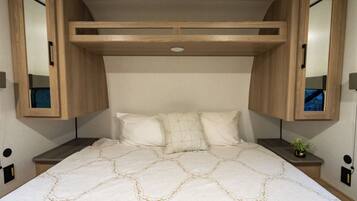 A bed with a patterned bedspread, two bedside tables, a nightstand, and a headboard with built-in lighting.