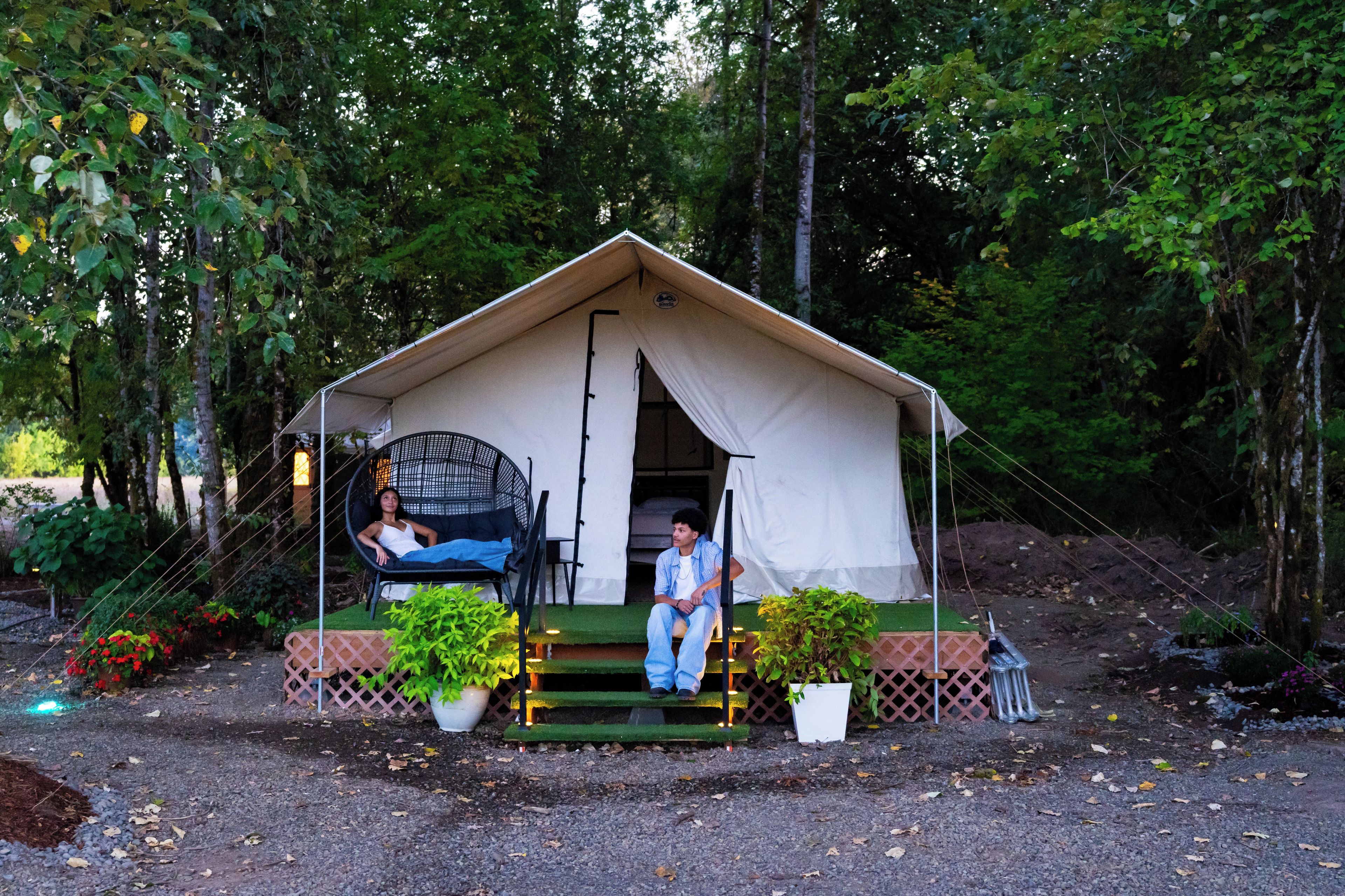 A tent with a covered porch, two chairs, and potted plants.