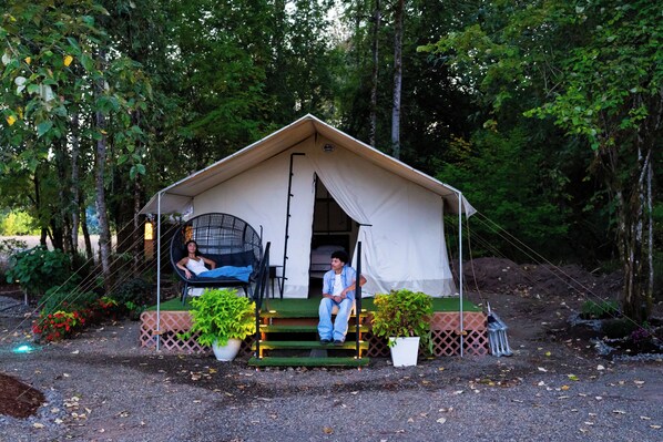 A tent with a covered porch, two chairs, and potted plants. - New Leaf Greenhouse (Cornelius)
