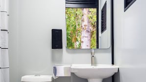 A bathroom with a toilet, sink, and a window with a view of greenery. - New Leaf Greenhouse (Cornelius)