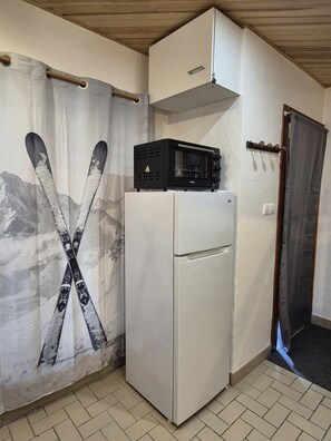 Eine kompakte Küche mit Kühlschrank, Mikrowelle und einem Vorhang mit Ski-Motiv.