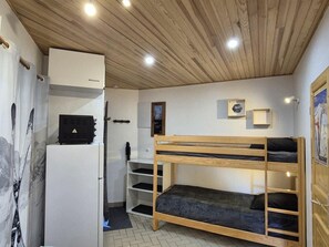 Ein kleines Zimmer mit Etagenbett, weißem Kleiderschrank, Schreibtisch und einer kleinen Regalwand.