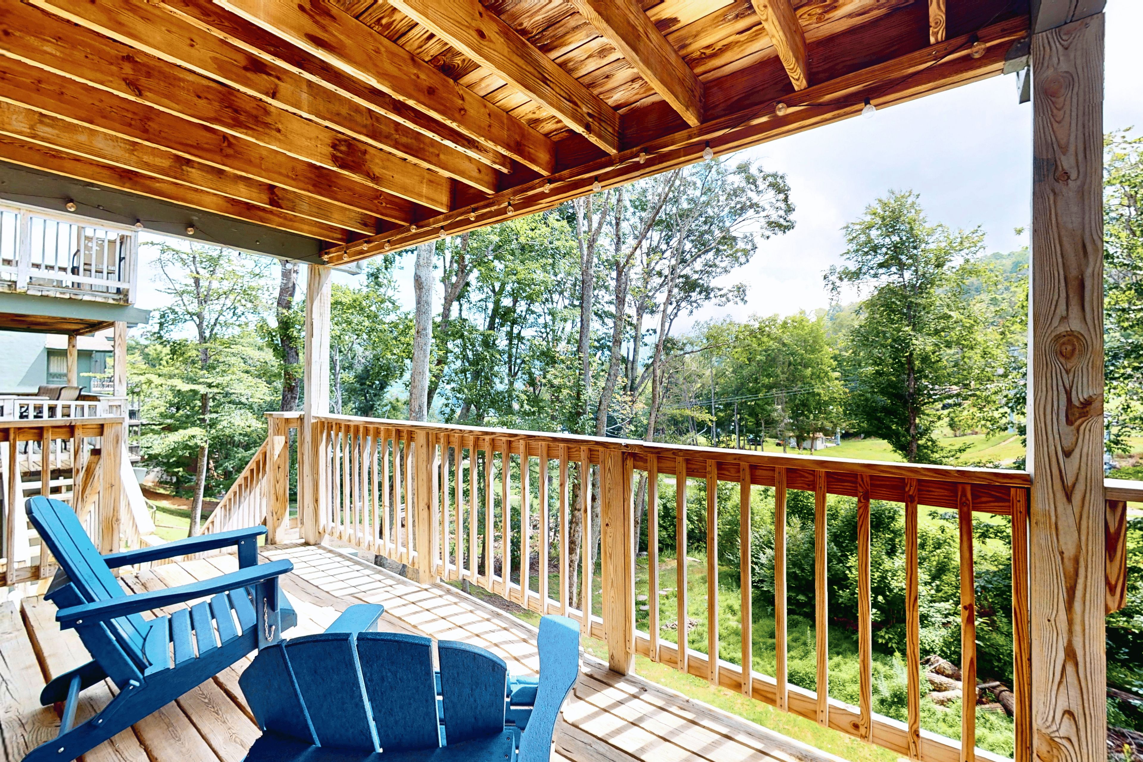 A wooden deck with a railing, two blue chairs, and a view of a forested area.