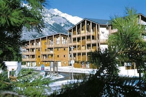 A multi-story wooden building with balconies, set against a snowy mountain backdrop. - 300m from ski slopes, 1st floor, balcony, parking, tv, ski locker, 45m², La Norma (Villarodin-Bourget)
