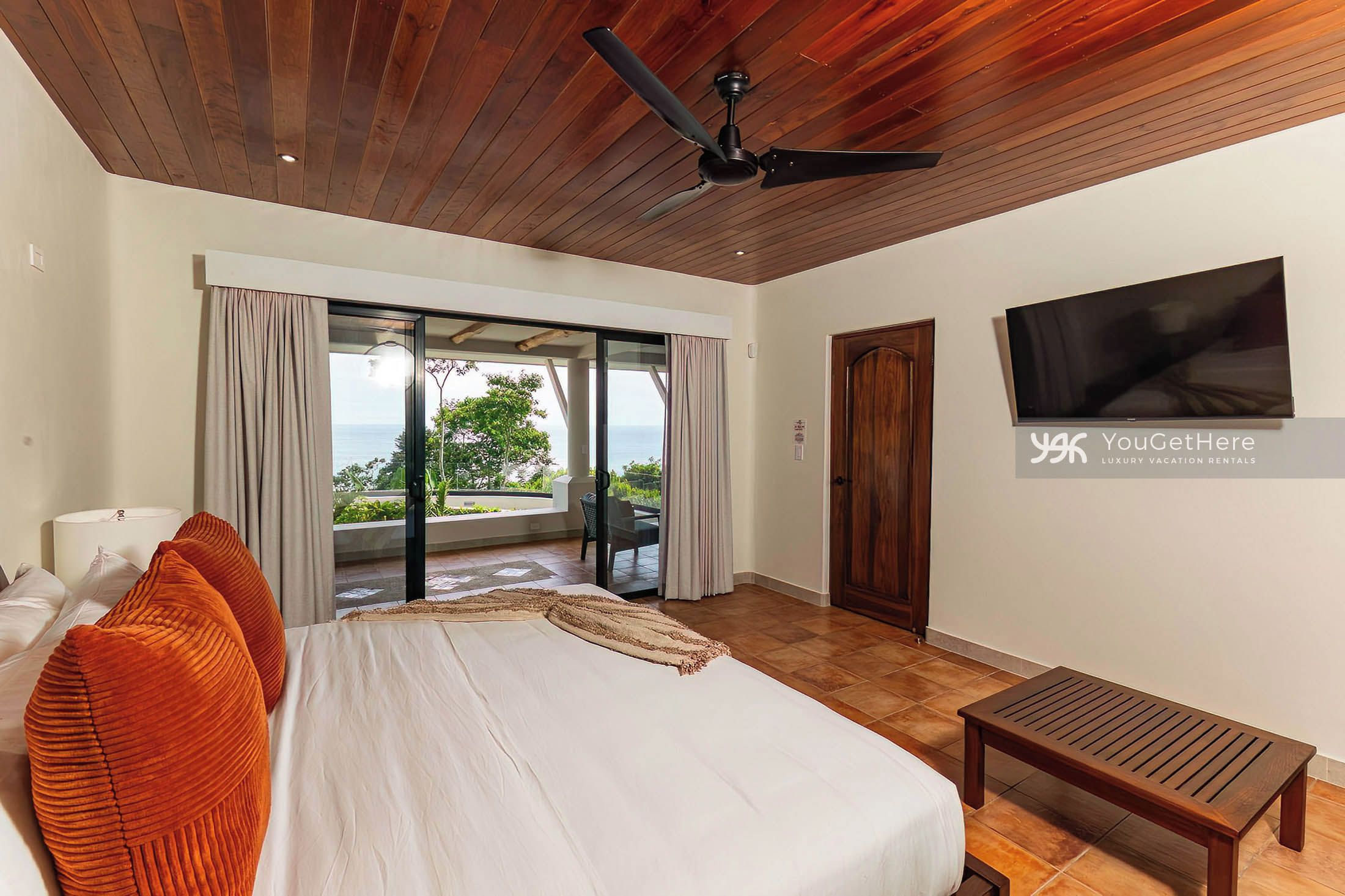Un dormitorio con cama, televisor, ventilador de techo de madera y vistas al exterior.