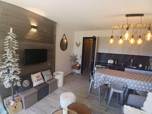A modern living room with a flat-screen TV, a sofa with decorative pillows, a dining area with a table and chairs, and a kitchen with cabinets and a countertop. - 250m from ski slopes, balcony, tv, ski locker, 28m², Alpe d'Huez (L'Alpe d'Huez)