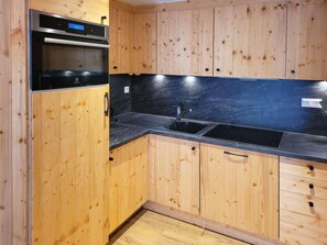 A kitchen with wooden cabinets, a black countertop, and a stainless steel oven. - Terrace, parking, tv, ski locker, 65m², Les Orres (Les Orres)