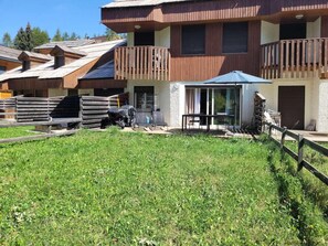 A multi-story building with balconies, a covered outdoor seating area, and a grassy yard. - Terrace, parking, tv, ski locker, 65m², Les Orres (Les Orres)