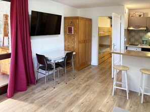 A compact kitchen with a dining area, wooden cabinets, a TV mounted on the wall, and a red curtain. - 50m from ski slopes, 4th floor, balcony, 30m², Les Orres (Les Orres)