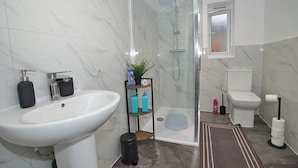 Casa de banho moderna com lavatório branco, sanita e cabine de duche em vidro.