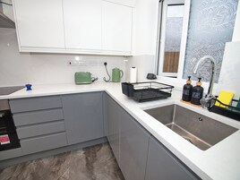Una cocina moderna con armarios blancos, un lavamanos de acero inoxidable y un ventanal con vidrio esmerilado.