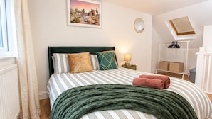 Cama bem arrumada com roupa de cama listrada e um cobertor verde, uma luminária de cabeceira e uma pintura na parede.