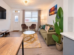 Una sala de estar moderna con un sofá, dos sillones, una mesa de centro y un televisor.