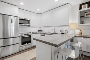 A modern kitchen with stainless steel appliances, a central island, and white cabinetry. - Snowlion Vail - Pool, Near Shuttle & Village (Vail)