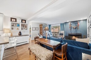 A modern living room with a fireplace, a dining area with a wooden table, and a blue sofa. - Snowlion Vail - Pool, Near Shuttle & Village (Vail)