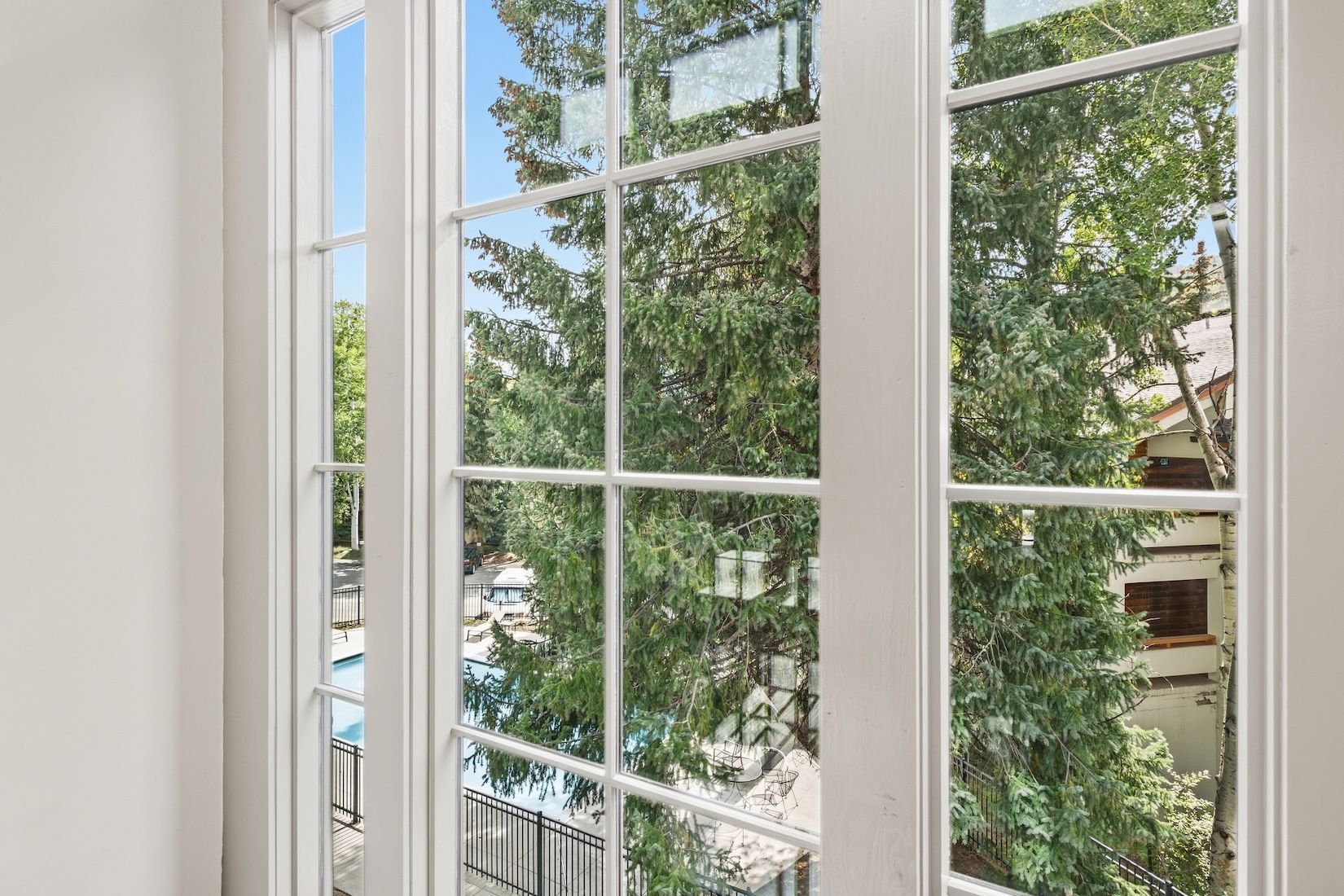 A view through a window with a white frame, looking out onto a balcony with a railing and trees.