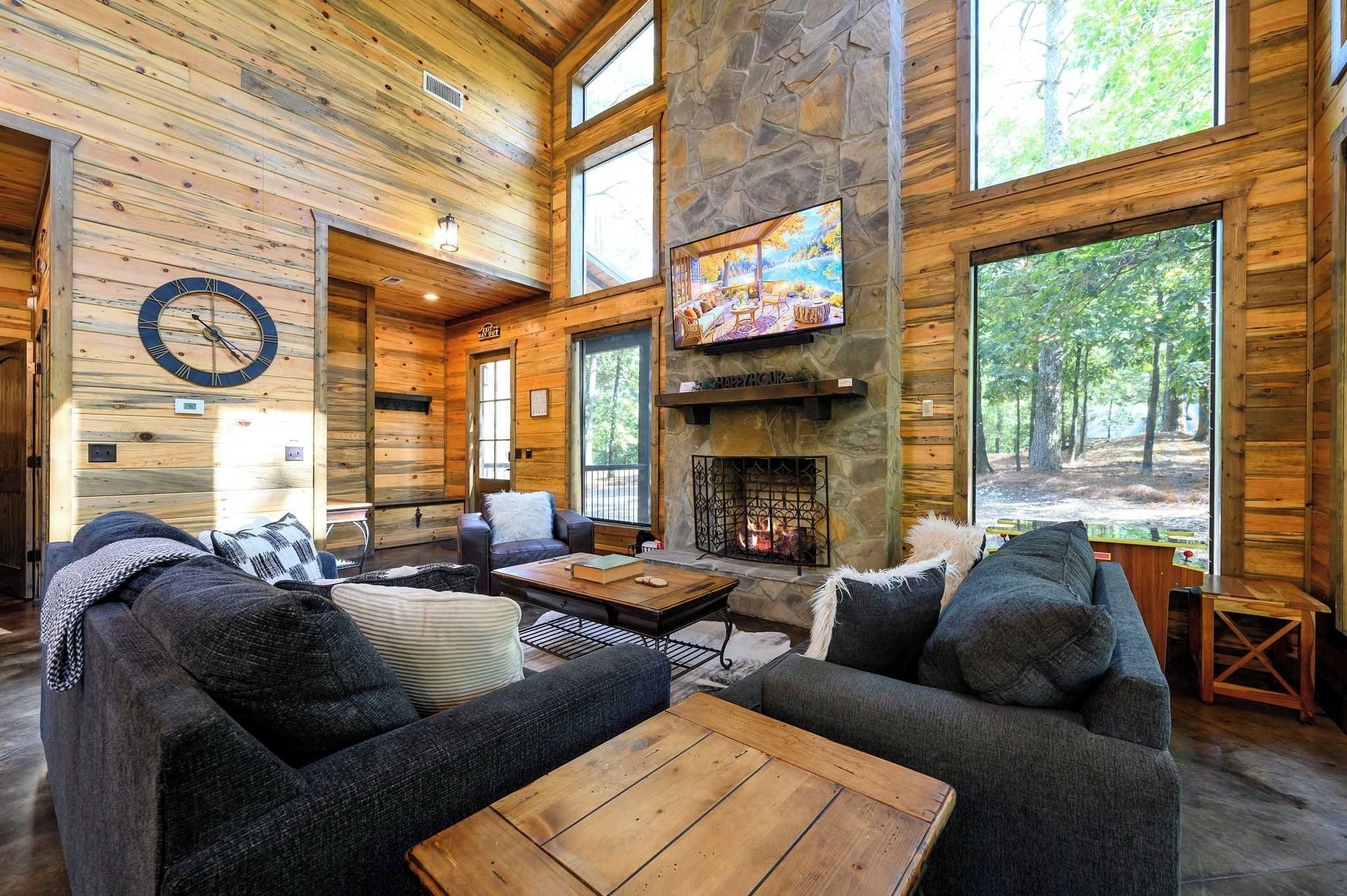 A log cabin interior with a fireplace, large windows, and a cozy seating area.