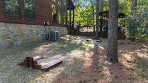 A wooden cabin with a stone wall, a wooden deck, and a staircase leading to a covered area. - Happy Hours - Hot Tub, Fire Pit, Coziness (Broken Bow)
