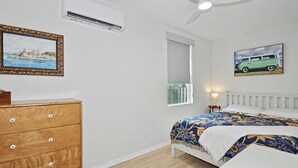 Et soveværelse med seng, kommode, aircondition og et billede på væggen.