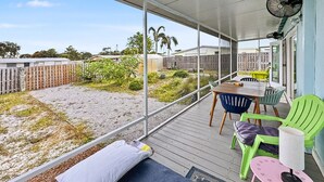 Et overdækket udendørs område med et bord, stole, en ventilator og udsigt til en have.