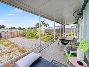 Een overdekt buitengebied met een tafel, stoelen, een ventilator en uitzicht op een achtertuin.
