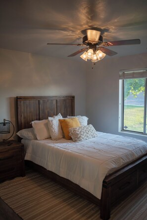 A bedroom with a bed, a nightstand, a lamp, a ceiling fan, and a window with a view. - Luxury Bluffdale Retreat Theater•Hot Tub •Sauna (Bluffdale)