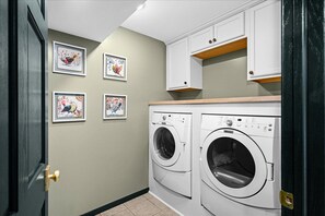 A laundry room with two front-loading washing machines, a wooden countertop, and wall-mounted cabinets.