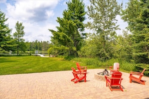 A paved outdoor area with red Adirondack chairs and a fire pit.