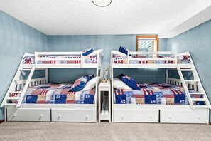 A room with two bunk beds, each with a storage drawer and a small bedside table.