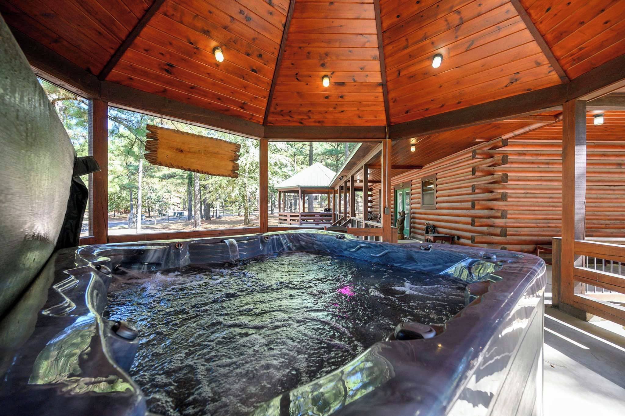 A hot tub in a wooden cabin with a covered porch and a view of the surrounding forest.