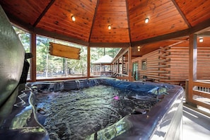 Un jacuzzi en una cabaña de madera con un porche cubierto y vistas al bosque circundante.