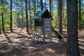 Un parque infantil con una estructura para escalar y un tobogán, rodeado de árboles.