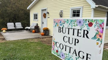 Une maison avec une pancarte indiquant « BUTTER CUP COTTAGE » et une véranda avec des chaises et des citrouilles.