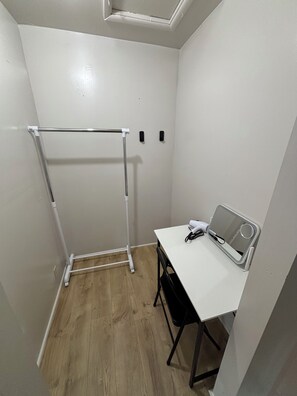 Una habitació petita amb escriptori blanc, cadira, radiador blanc i sortida de ventilació al sostre.