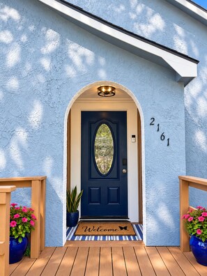 Una puerta azul con un panel de vidrio decorativo, felpudo y los números '2161' en la pared.