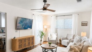Una sala de estar moderna con ventilador de techo, un cuadro grande, un mueble de madera, una mesa de centro redonda y un sofá color beige.