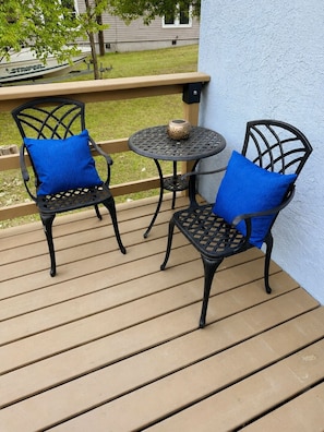 En terrasse med to stole og et lille bord, en pynteting på bordet, og et hus i baggrunden.