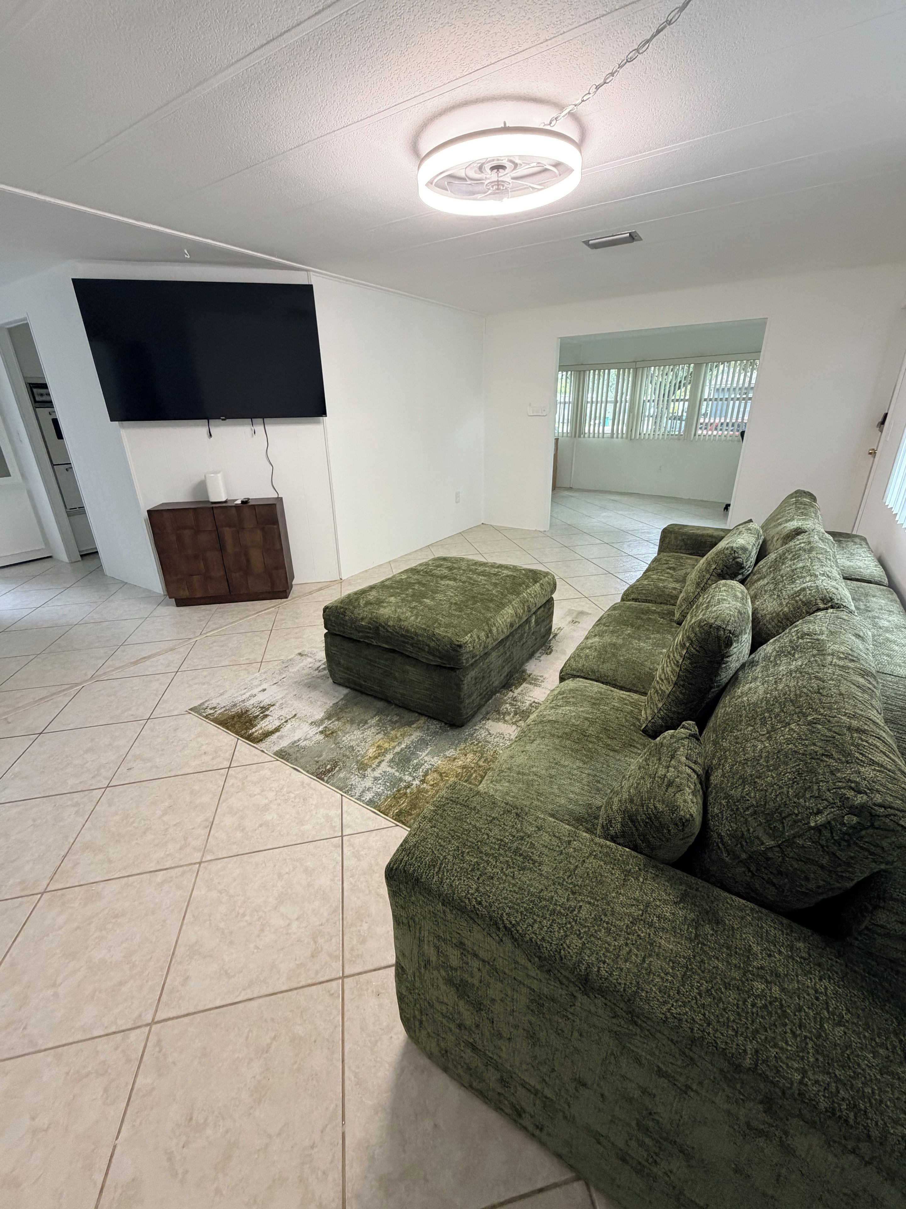 A living room with a sectional sofa, a flat-screen TV, a wooden cabinet, and a patterned rug.