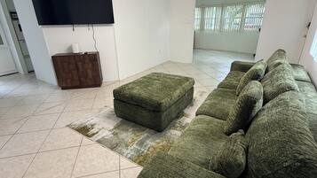 A living room with a sectional sofa, a flat-screen TV, a wooden cabinet, and a patterned rug.
