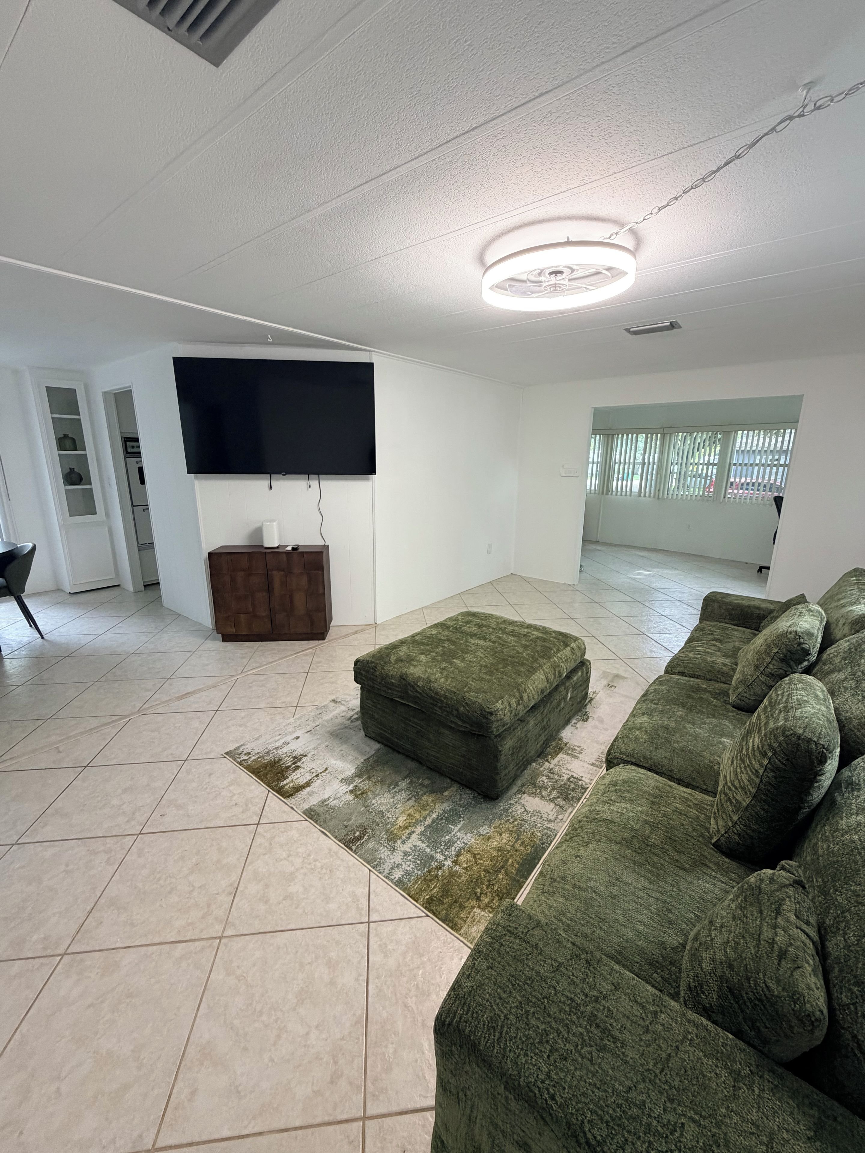 A spacious living room with a large sectional sofa, a flat-screen TV mounted on the wall, and a wooden cabinet.
