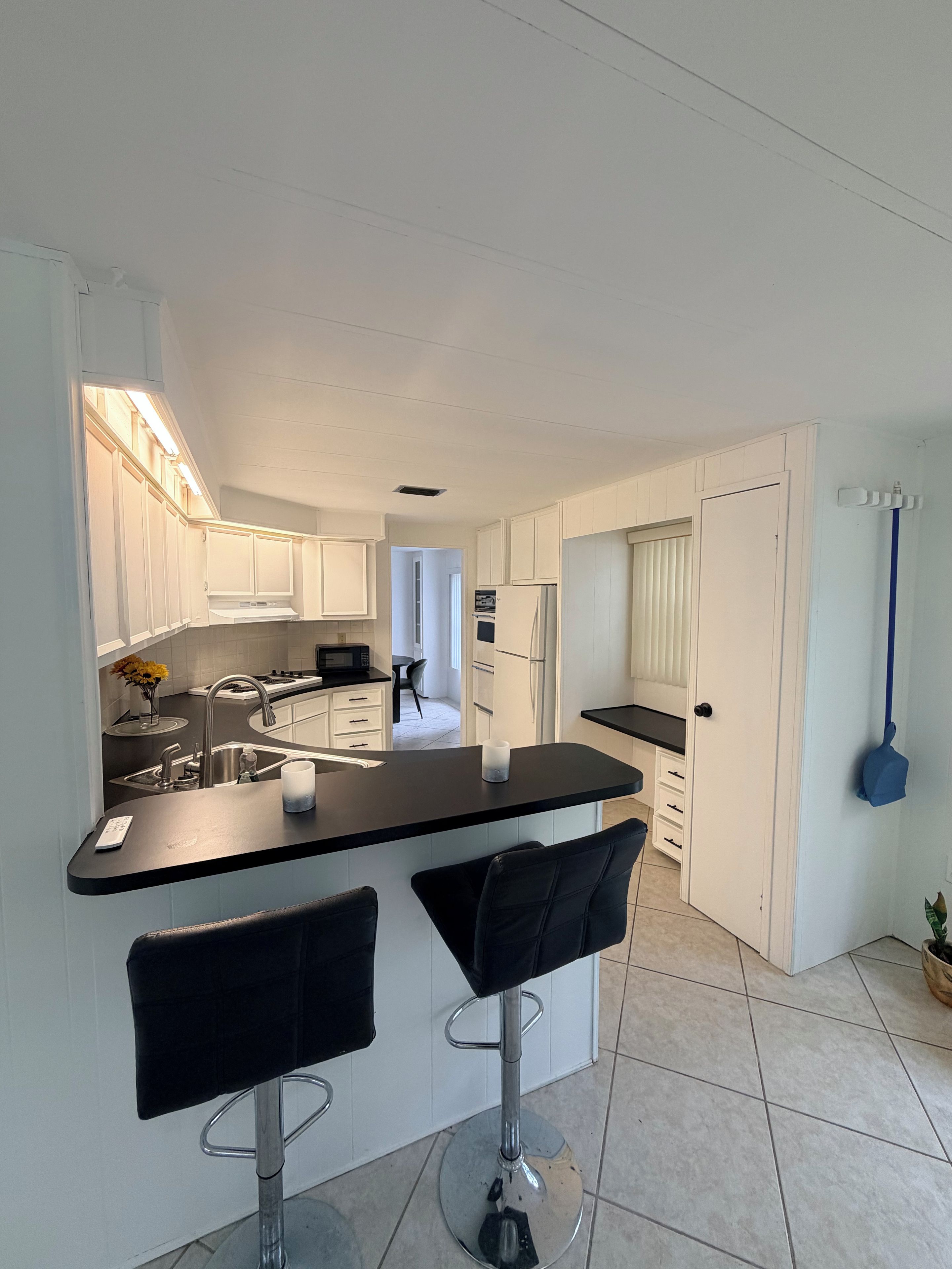 A modern kitchen with white cabinetry, a black countertop, and two bar stools.