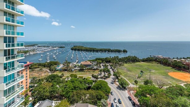 A high-rise hotel overlooking a marina with boats, a baseball field, and a clear sky. - Bay View Beauty: 1/1.5 Bath Condo in Coconut Grove! Parking Included (Miami)