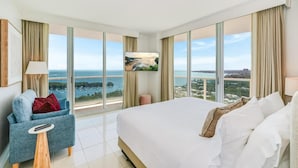 A hotel room with a large bed, a blue armchair, a TV, and a view of a coastal landscape. - Bay View Beauty: 1/1.5 Bath Condo in Coconut Grove! Parking Included (Miami)