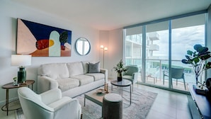 Sala de estar moderna com sofá, mesa de centro e vista para a água através de grandes janelas.