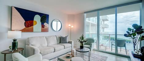 A modern living room with a sofa, coffee table, and a view of a body of water through large windows.