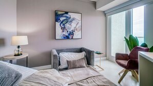 Quarto moderno com cama, cadeira, mesa de apoio, abajur e uma grande janela com vista.