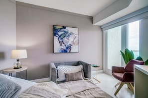 A modern bedroom with a bed, a chair, a side table, a lamp, and a large window with a view. - Direct Bayview One Bedroom Condo in Coconut Grove-includes Parking (Miami)